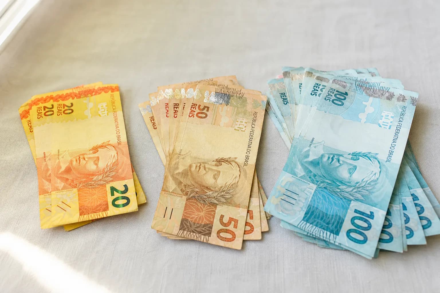 Três montes de notas de real de frente, cada um maior que o anterior